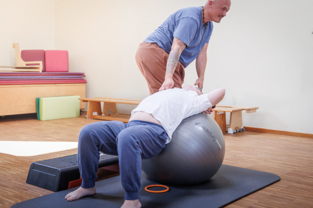 Physiotherapeut betreut eine Uebung auf dem Gymnastikball